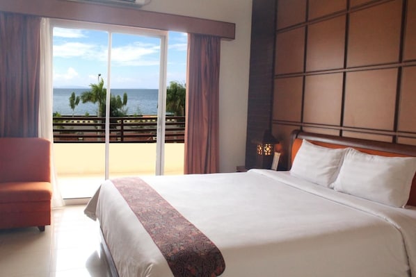 A hotel room with a large bed, a chair, a view of the ocean, and a balcony with a railing. - Sutan Raja Hotel Kolaka (Kolaka)