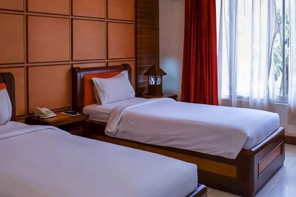 A hotel room with two beds, a nightstand with a lamp, and a window with curtains.