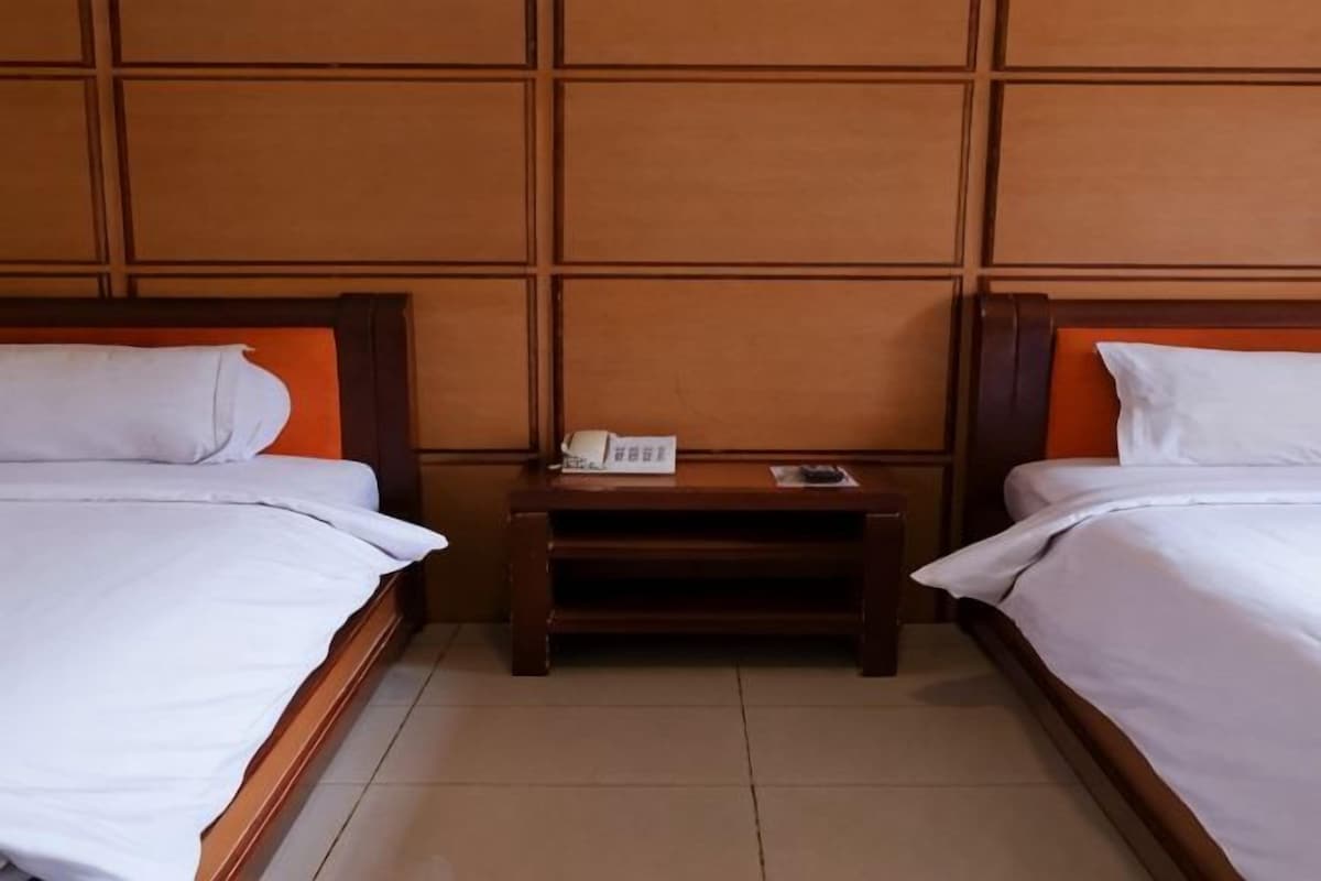 Una habitación de hotel con dos camas, una mesita de noche con teléfono y un cabecero de madera.
