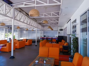Un amplio espacio interior con asientos color naranja, vigas estructurales blancas y lámparas colgantes.