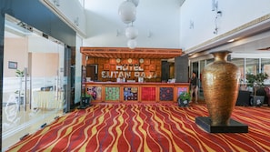 Un vestíbulo de hotel con una recepción, un jarrón grande y una alfombra estampada.