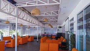 Een ruime lobby met oranje zitplaatsen, een hoog plafond met zichtbare balken en grote ramen.