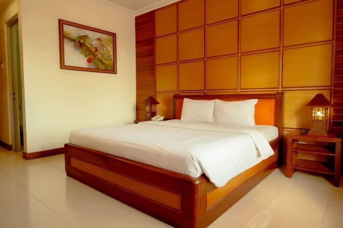 A hotel room with a wooden bed, a nightstand with a lamp, and a painting on the wall.