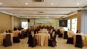 A conference room with round tables, chairs, and a podium. - Sutan Raja Hotel Kolaka (Kolaka)