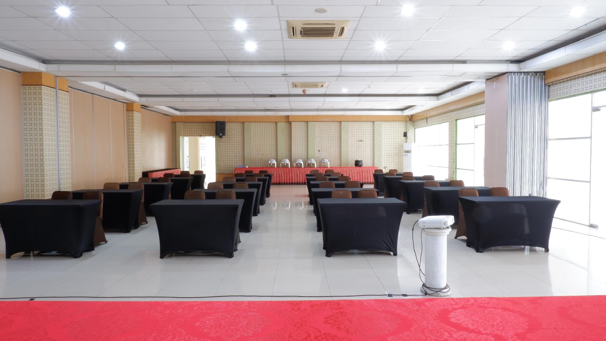 A conference room with rows of tables and chairs, a podium at the front, and large windows on one side.