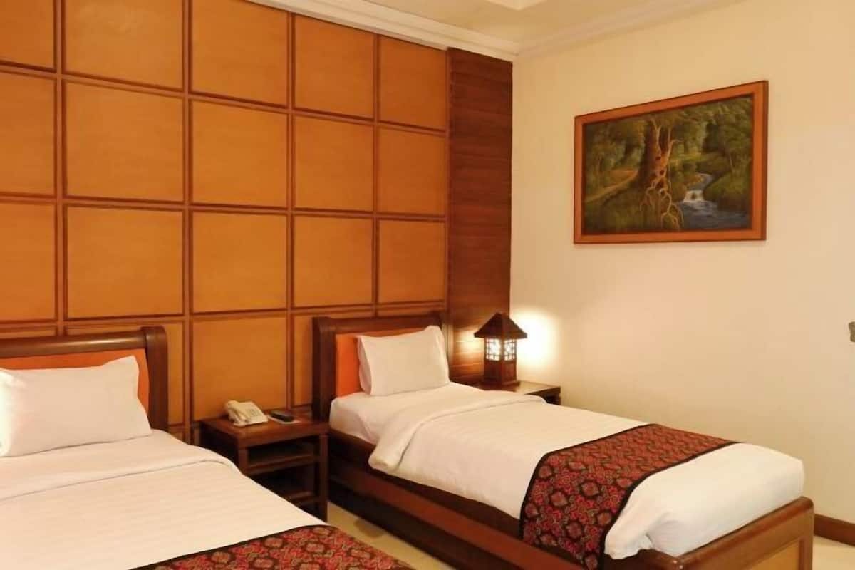 A hotel room with two beds, a wooden headboard, a nightstand with a lamp, and a painting on the wall.