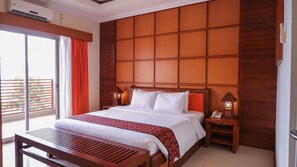 A hotel room with a large bed, a wooden headboard, a bedside table with a lamp, and a view of the outside balcony. - Sutan Raja Hotel Kolaka (Kolaka)