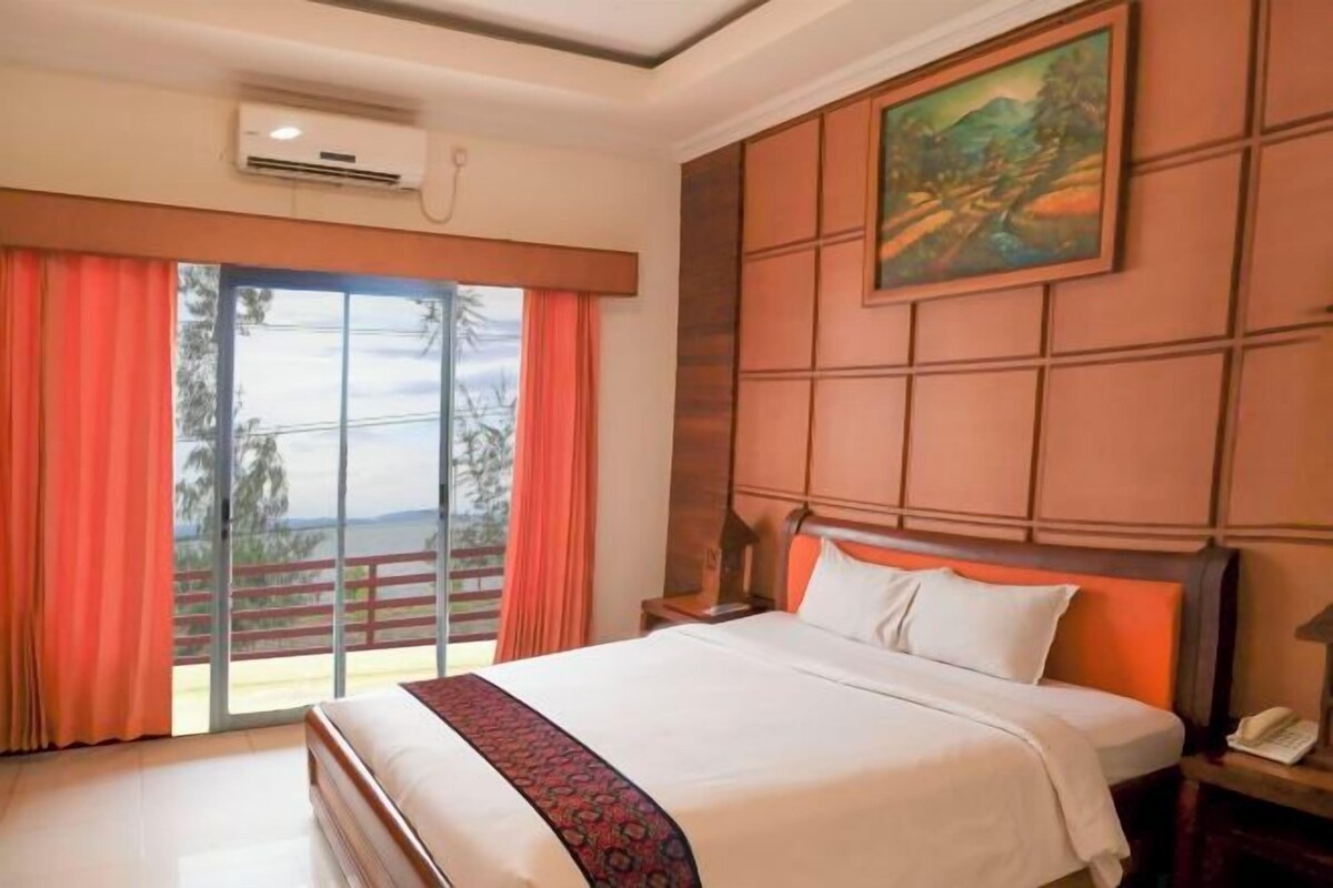 A hotel room with a large bed, a painting on the wall, and a view through the window.