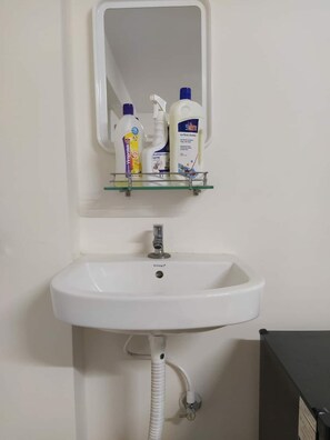 Ein weißes Waschbecken mit Spiegel darüber, eine Glasablage für Toilettenartikel und ein weißer Schlauch, der an das Waschbecken angeschlossen ist.