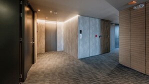 Un passadís modern amb sòl de moqueta, parets de fusta i una porta amb un senyal vermell de sortida d'emergència.