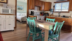 A kitchen with wooden cabinets, a dining table with chairs, and a microwave on a cabinet. - Sunset Cottage on Pillar Point (Dexter)
