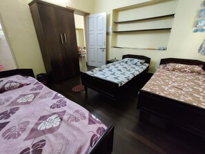Two single beds with floral-patterned bedding, a wardrobe, and a shelf unit are featured in this cozy room.