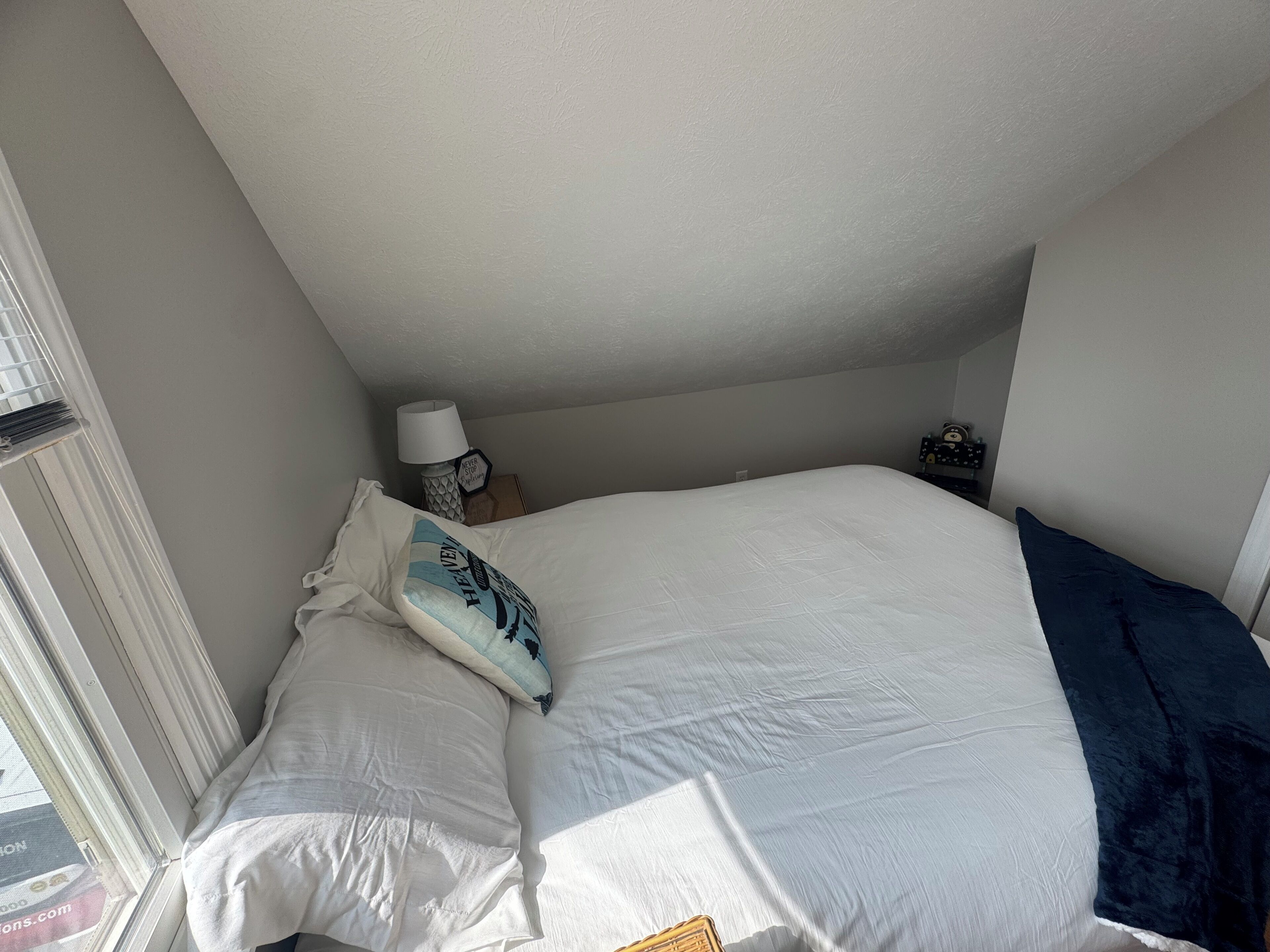 Et soveværelse med en stor seng, et vindue og et natbord med en lampe.