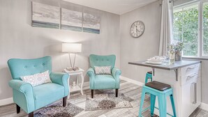 A modern living room with two teal armchairs, a small white table, a clock, and a window with a view of greenery. - Lighthouse Inn & Suites Extended Stay
Boutique Hotel I-69 Exit 334 (Waterloo)