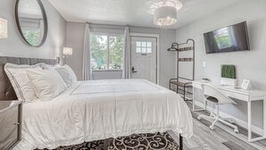 A bedroom with a bed, a desk, a chair, a television, and a window. - Lighthouse Inn & Suites Extended Stay
Boutique Hotel I-69 Exit 334 (Waterloo)