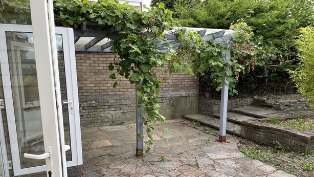 A stone patio with a brick wall and a wooden pergola covered in green vines. - Cheerful 3 Bedroomed house,with parking and free intern free (Luton)