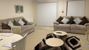 A living room with two beige sofas, a white dining table, and a small coffee table. - Cheerful 3 Bedroomed house,with parking and free intern free (Luton)