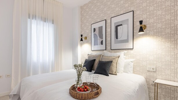 A modern hotel room with a large bed, white bedding, a decorative basket with flowers, and framed artwork on the wall. - ChezmoiHomes Angel 1 1BR (Granada)