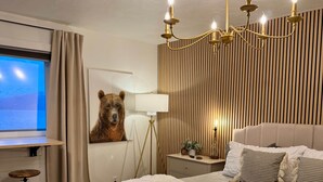 Un dormitorio con una cama grande, un escritorio, un cuadro de un oso en la pared, una araña y vistas a la montaña a través de la ventana.