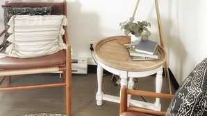 Una habitación acogedora con una silla de madera, una mesita redonda con una lámpara y un cuadro de un oso colgado en la pared.