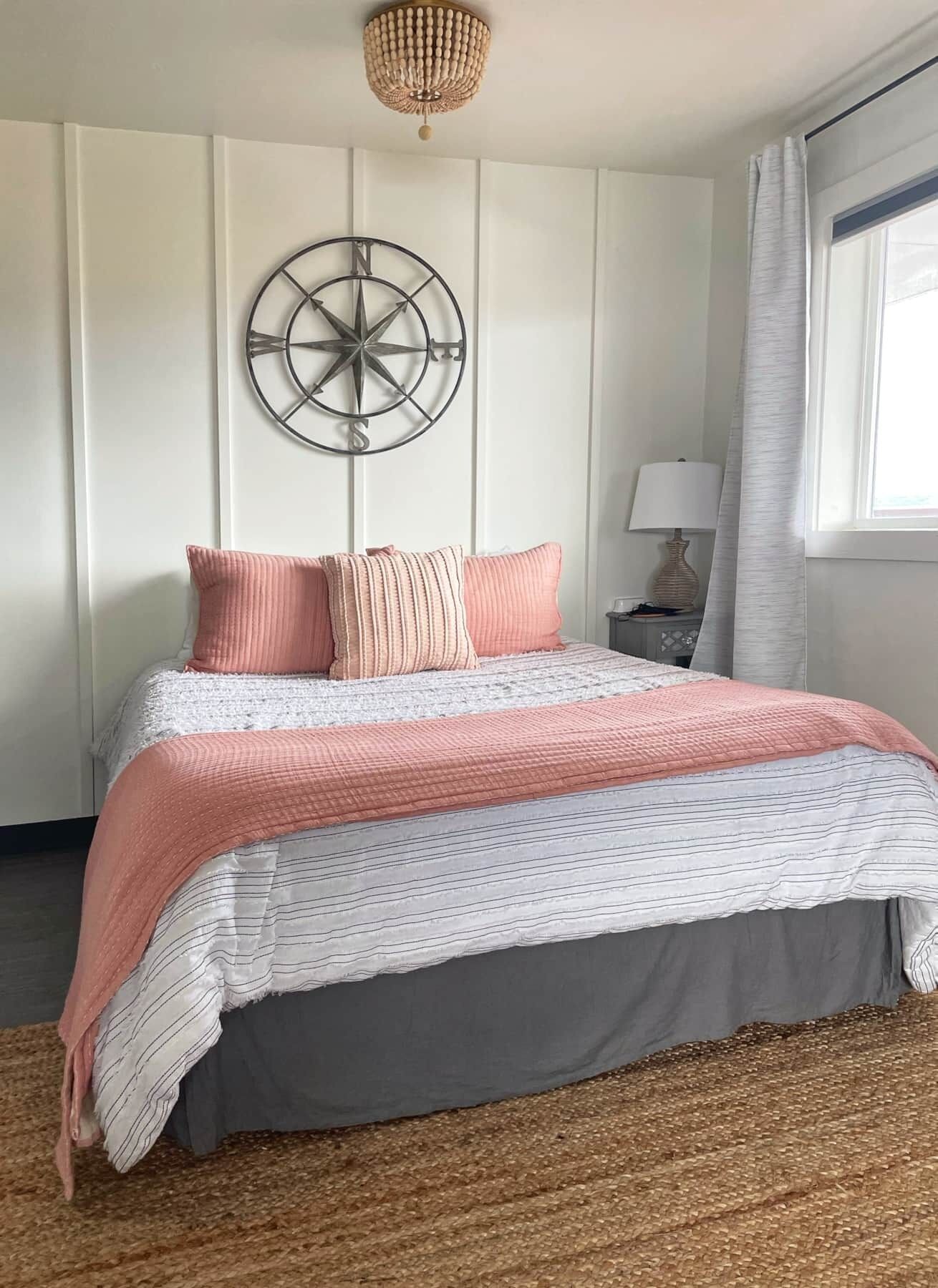 A bedroom with a bed, a wall-mounted compass decoration, a lamp, and a window with curtains.