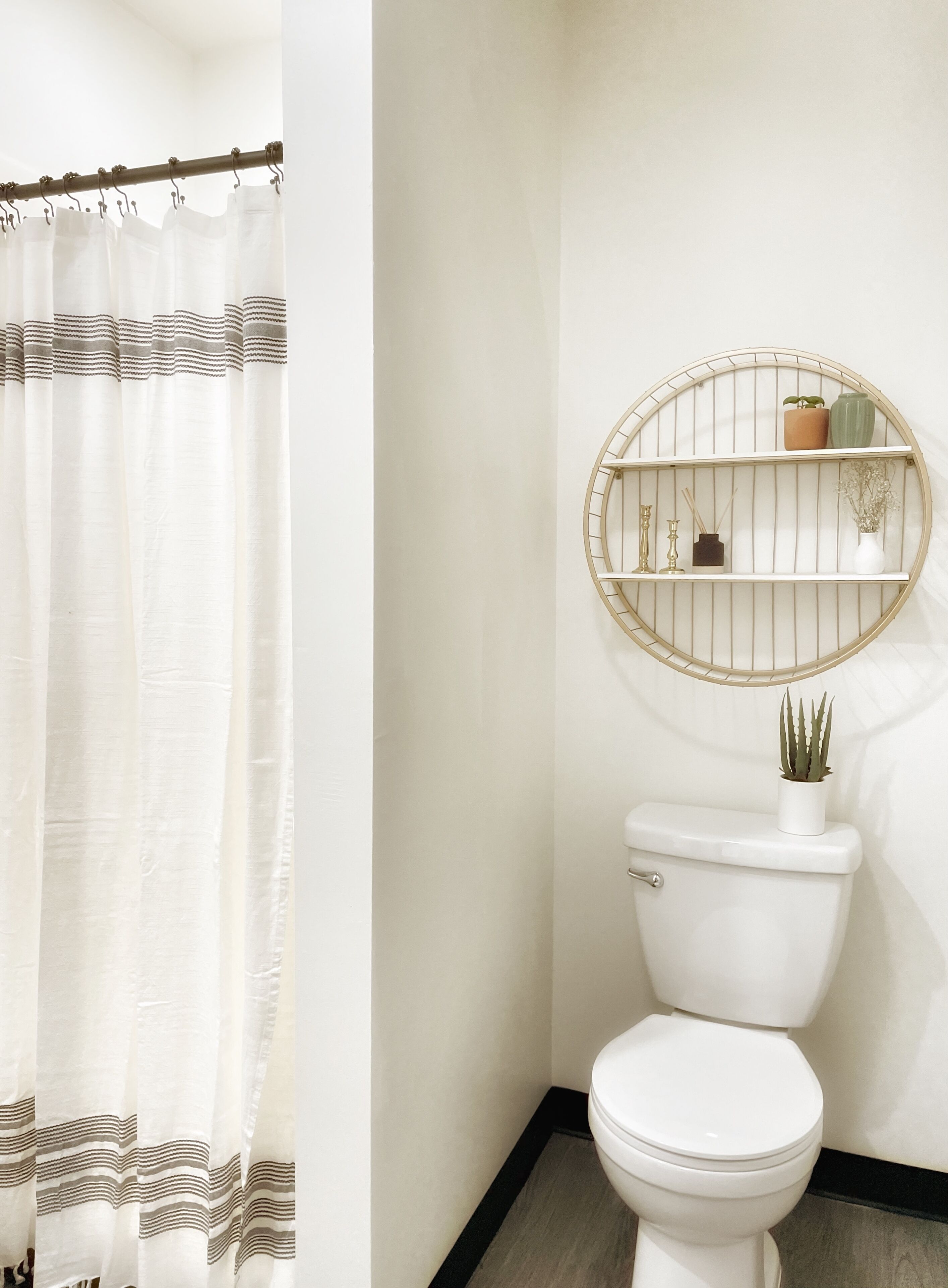A bathroom with a white toilet, a round shelf with plants, and a striped shower curtain.