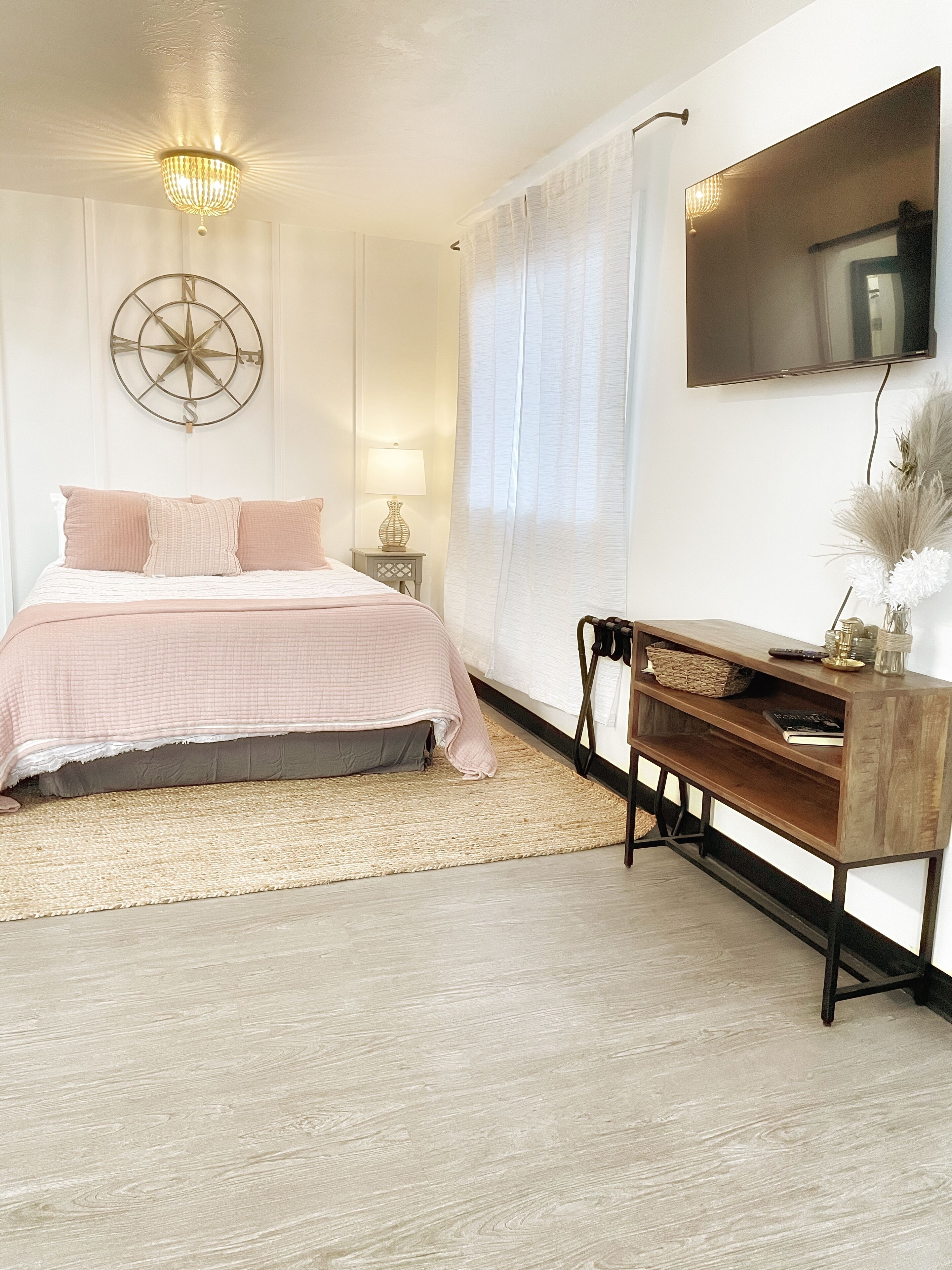 A bedroom with a bed, bedside table, lamp, and a mounted TV.