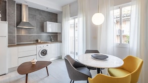 Uma cozinha moderna com máquina de lavar embutida, sala de jantar com mesa redonda e cadeiras, e janelas amplas com cortinas.