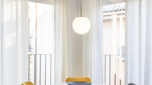 A round table with a bowl, surrounded by two yellow and two grey chairs, in a room with white curtains and a hanging light fixture. - ChezmoiHomes Angel 1 2BR (Granada)
