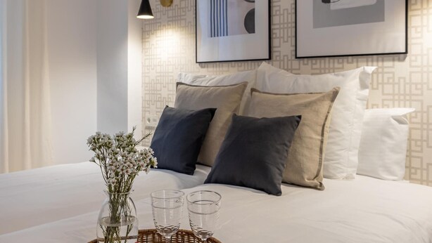 A neatly arranged bedroom with a bed, pillows, a vase with flowers, and two glasses on a tray. - ChezmoiHomes Angel 1 2BR (Granada)