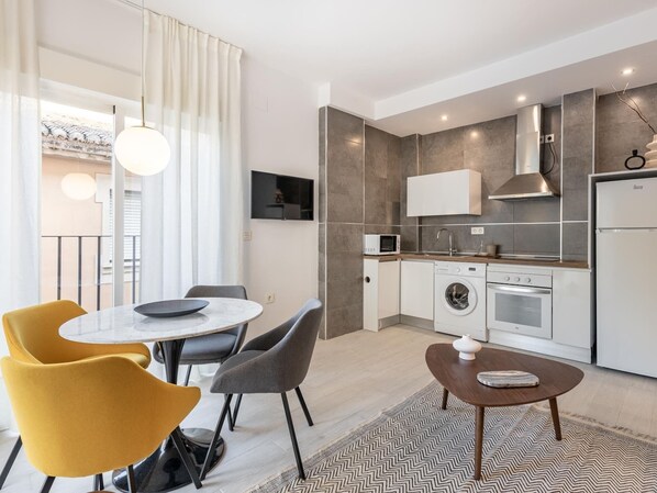 A modern kitchen with a microwave, oven, and washing machine. There is a dining area with a table and chairs.