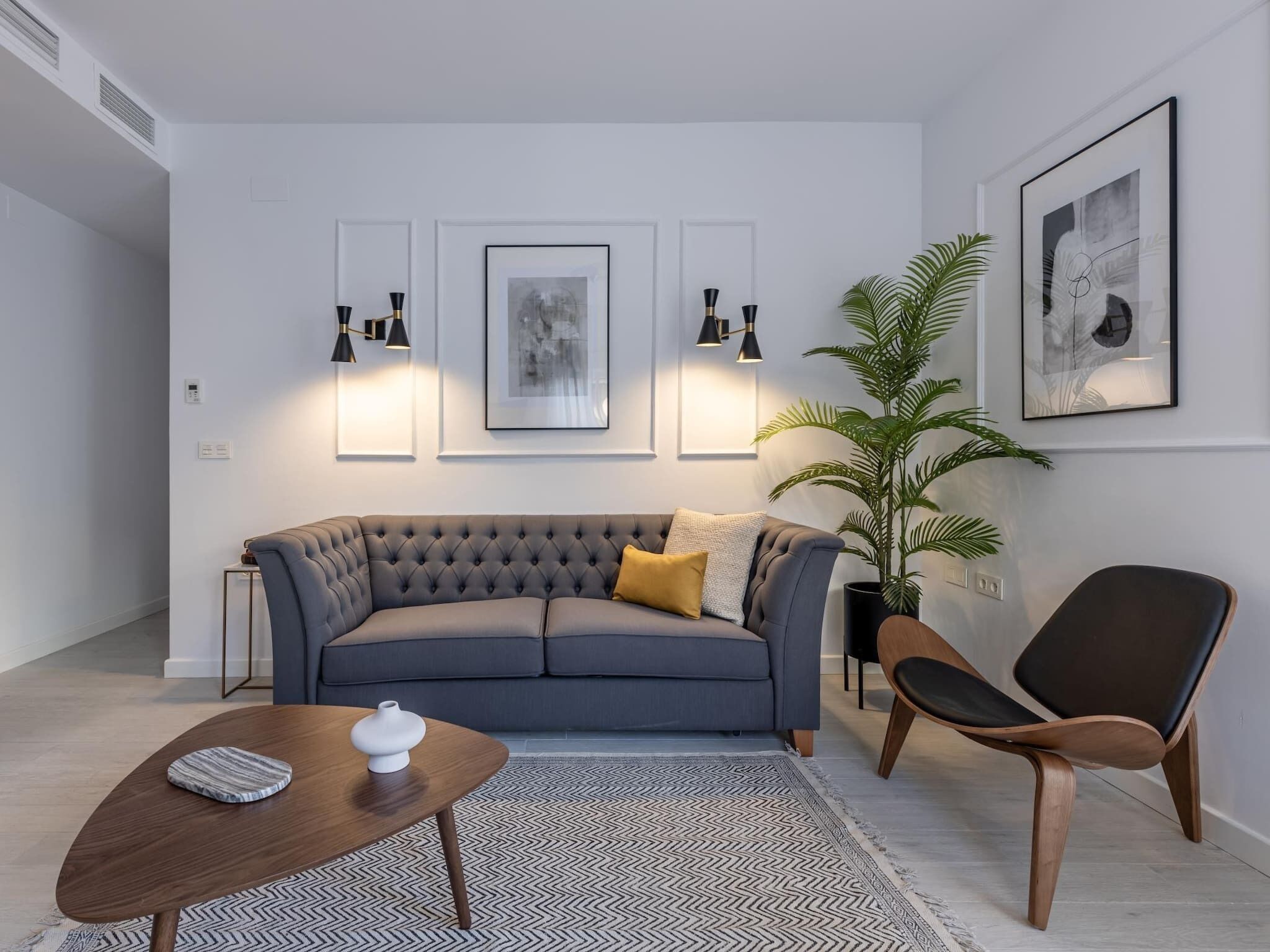 A modern living room with a grey sofa, a wooden coffee table, a black armchair, and a patterned rug.