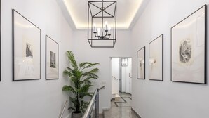 A modern hallway with framed artwork on the walls, a potted plant, and a staircase leading to another area. - ChezmoiHomes Angel 1 2BR (Granada)