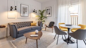 A modern living room with a grey sofa, a coffee table, and yellow chairs around a round table. - ChezmoiHomes Angel 1 2BR (Granada)