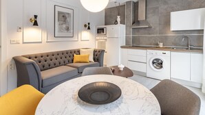 Un salón moderno con un sofá gris, una mesa redonda de mármol y una zona de cocina con lavadora.