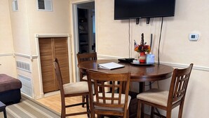 Un comedor con una mesa redonda, cuatro sillas de madera, un televisor montado en la pared y una pequeña decoración con la bandera estadounidense.