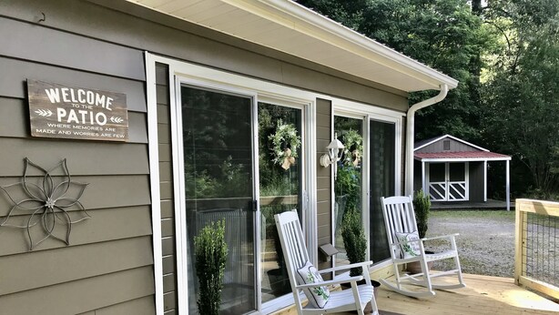 A covered patio with two rocking chairs, a welcome sign, and a small garden.