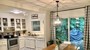 A modern kitchen with white cabinetry, a built-in oven, and a dining area with a wooden table and white chairs.