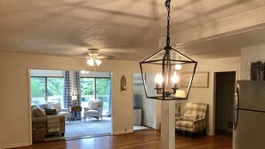 A spacious living area with a wooden floor, a dining table with a vase of flowers, and a kitchen area with a refrigerator.