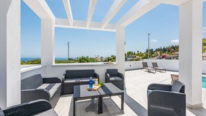 En tagterrasse med udendørs møbler, en pool og havudsigt.