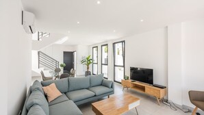 En moderne stue med en hjørnesofa, et træbord, et fjernsyn på et træstel og en trappe, der fører op til en etage.