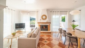 Un soggiorno con camino, televisore, divano, tavolo da pranzo con sedie e un balcone con vista.