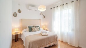 Una camera da letto con un letto, due lampade da comodino, un comodino, un condizionatore d'aria a parete e una finestra con tende.