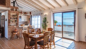 A dining area with wicker chairs and a table set for four, a brick fireplace, and a view of the sea through a large sliding glass door. - Villa María del Carmen Frigiliana by Ruralidays (Málaga)