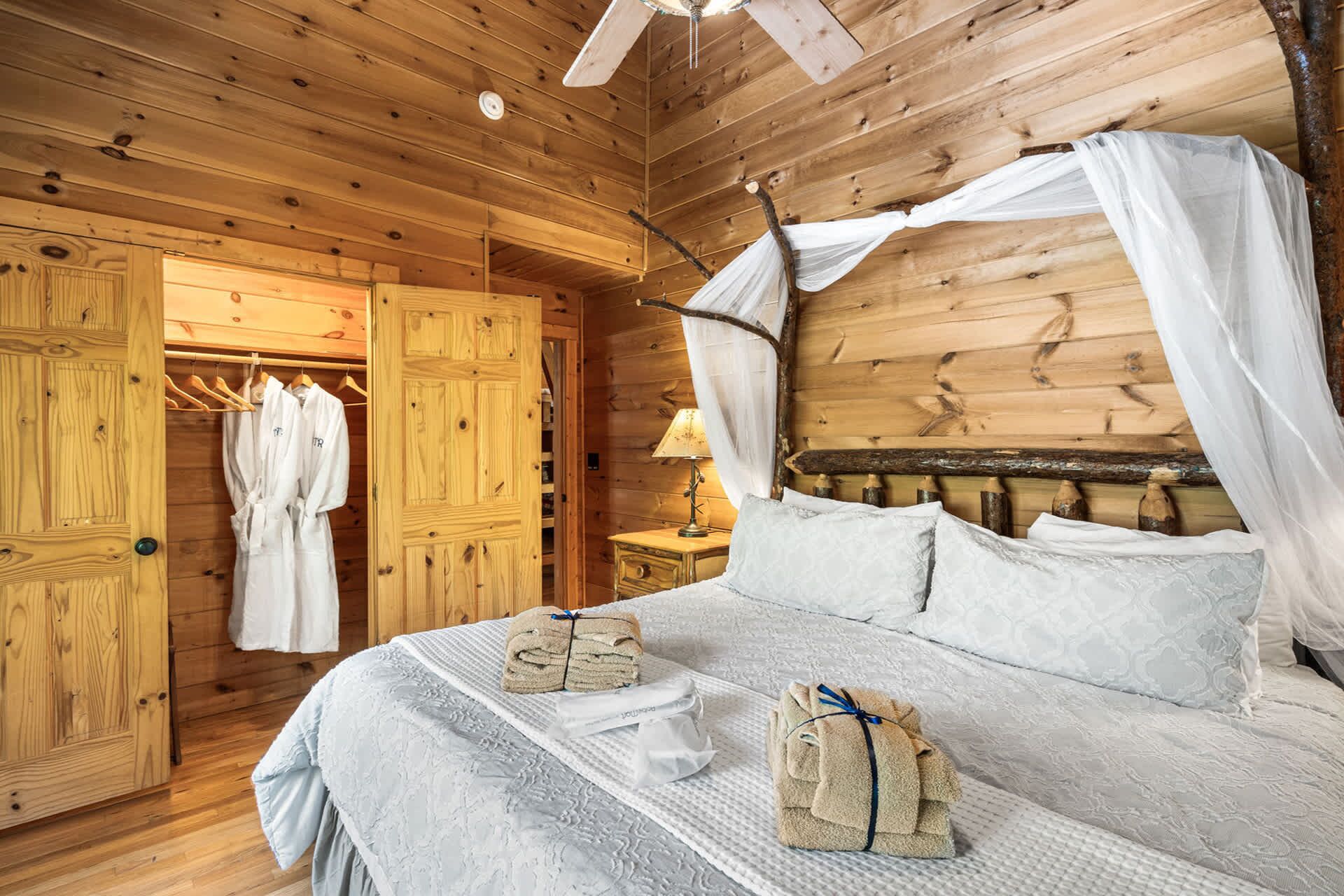 A wooden cabin bedroom with a canopy bed, a wardrobe, and a nightstand with a lamp.