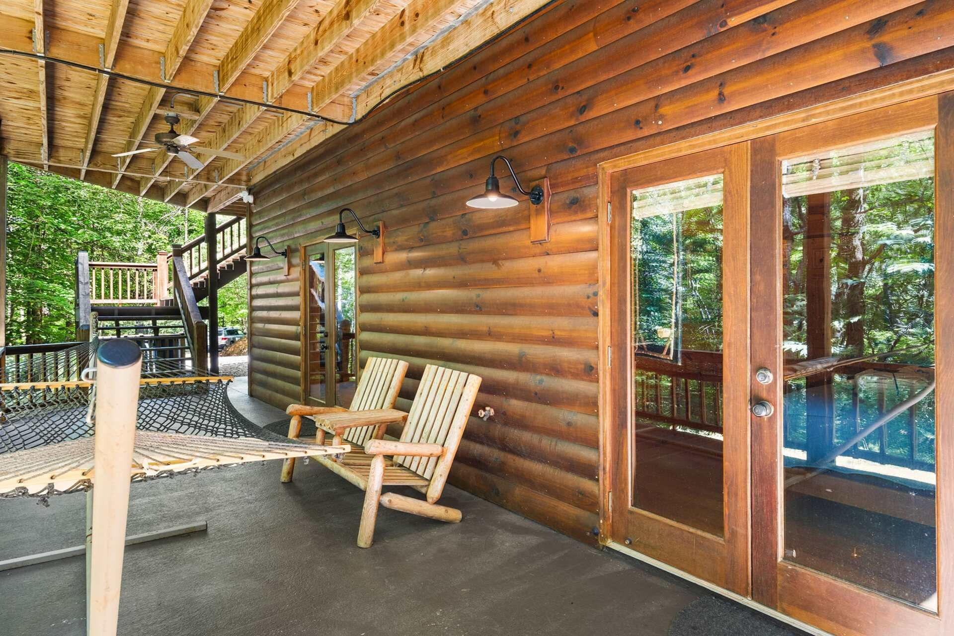 Une cabane en bois avec une véranda, deux chaises, un hamac et un escalier menant à une terrasse.