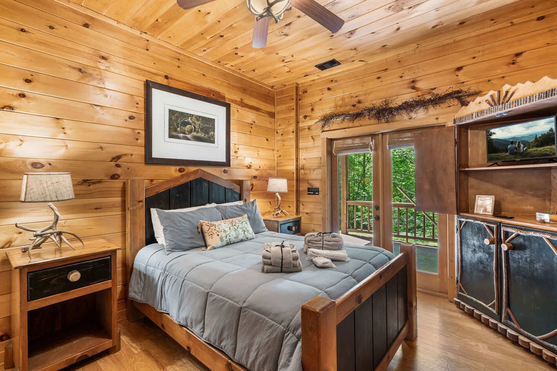 Camera da letto in una baita di legno, con un letto, comodini, un quadro incorniciato e una finestra vista panoramica.