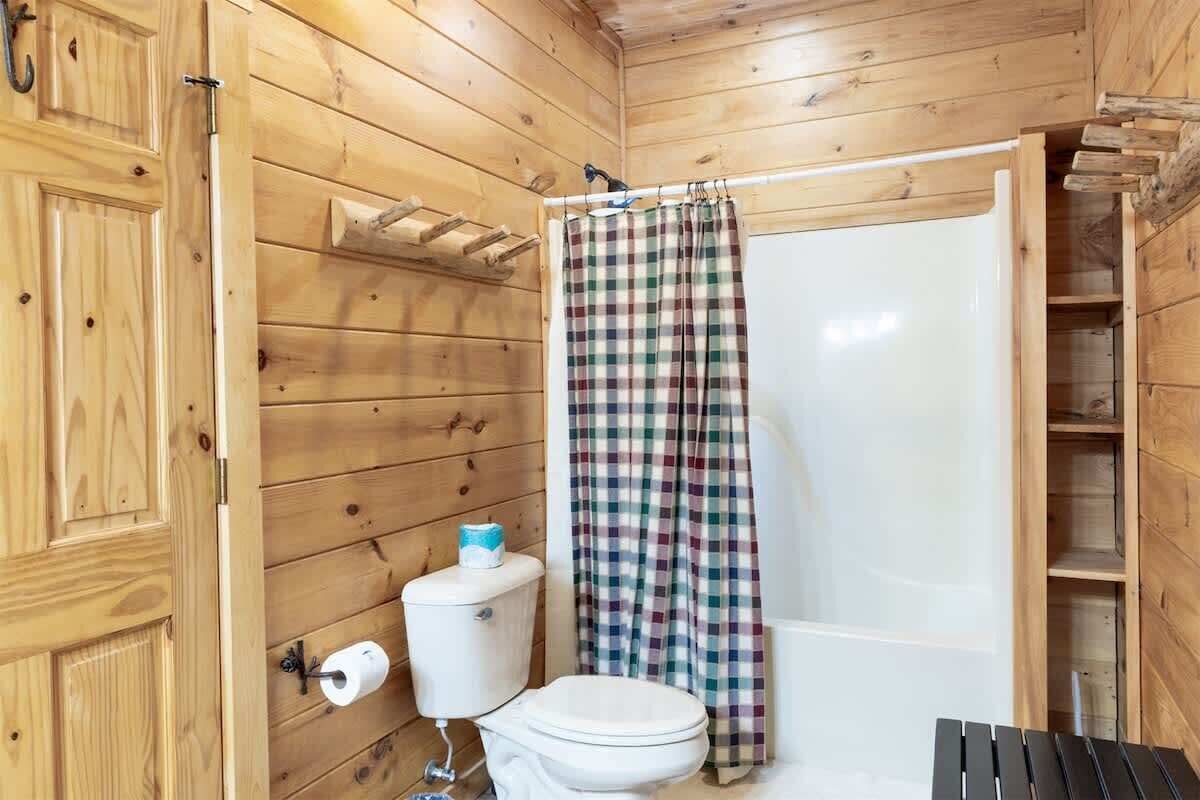 A wooden cabin bathroom with a toilet, a shower curtain, and a shelf above the toilet.