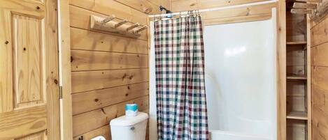 A wooden cabin bathroom with a toilet, a shower curtain, and a shelf above the toilet.
