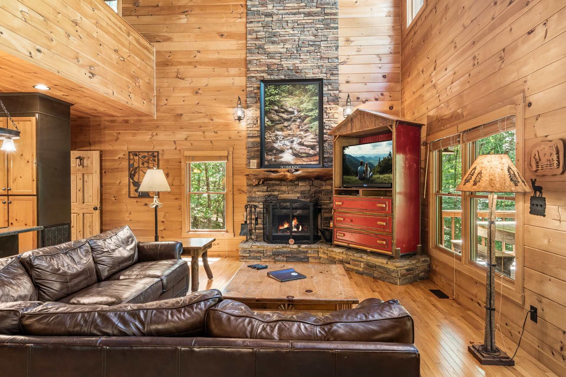 L’intérieur d’une cabane en rondins, avec une cheminée, un canapé en cuir, un plancher en bois et un mur en pierre.